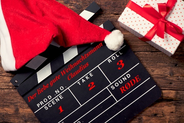 Filmklappe mit Aufschrift Der liebe gute Weihnachtsmann Claudius – Scene 1, Take 2, Roll 3, Sound: Rode – mit Weihnachtsmannmütze und Geschenkpaket