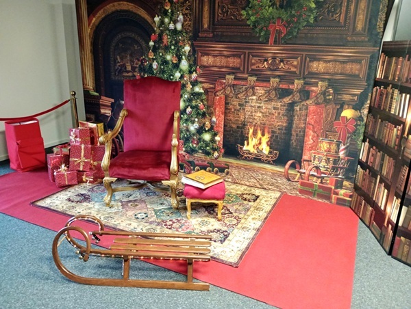Foto-Deko-Set im Innenraum: roter Thronsessel, Goldenes Buch auf Hocker, Fotodisplay mit Kaminzimmer-Motiv, Schlitten, Bibliotheks-Paravent rechts