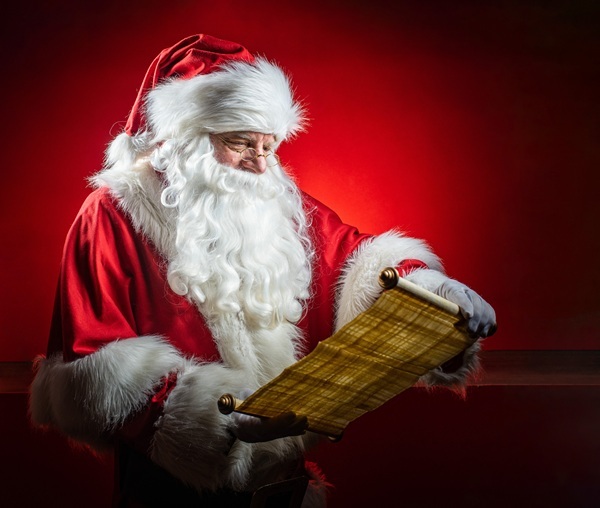 Weihnachtsmann Claudius liest konzentriert eine aufgerollte Schriftrolle, roter Studiohintergrund