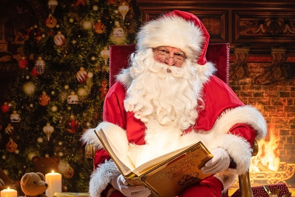 Weihnachtsmann Claudius im Thronsessel blickt in die Kamera mit Goldenem Buch, im Kaminzimmer